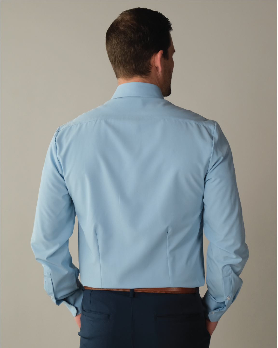 Back view of a man wearing a French blue button up shirt, tucked into navy blue pants.