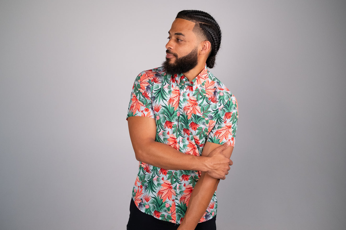 Tropical floral print shirt being worn by a model with one arm crossed over his body. Grey background.