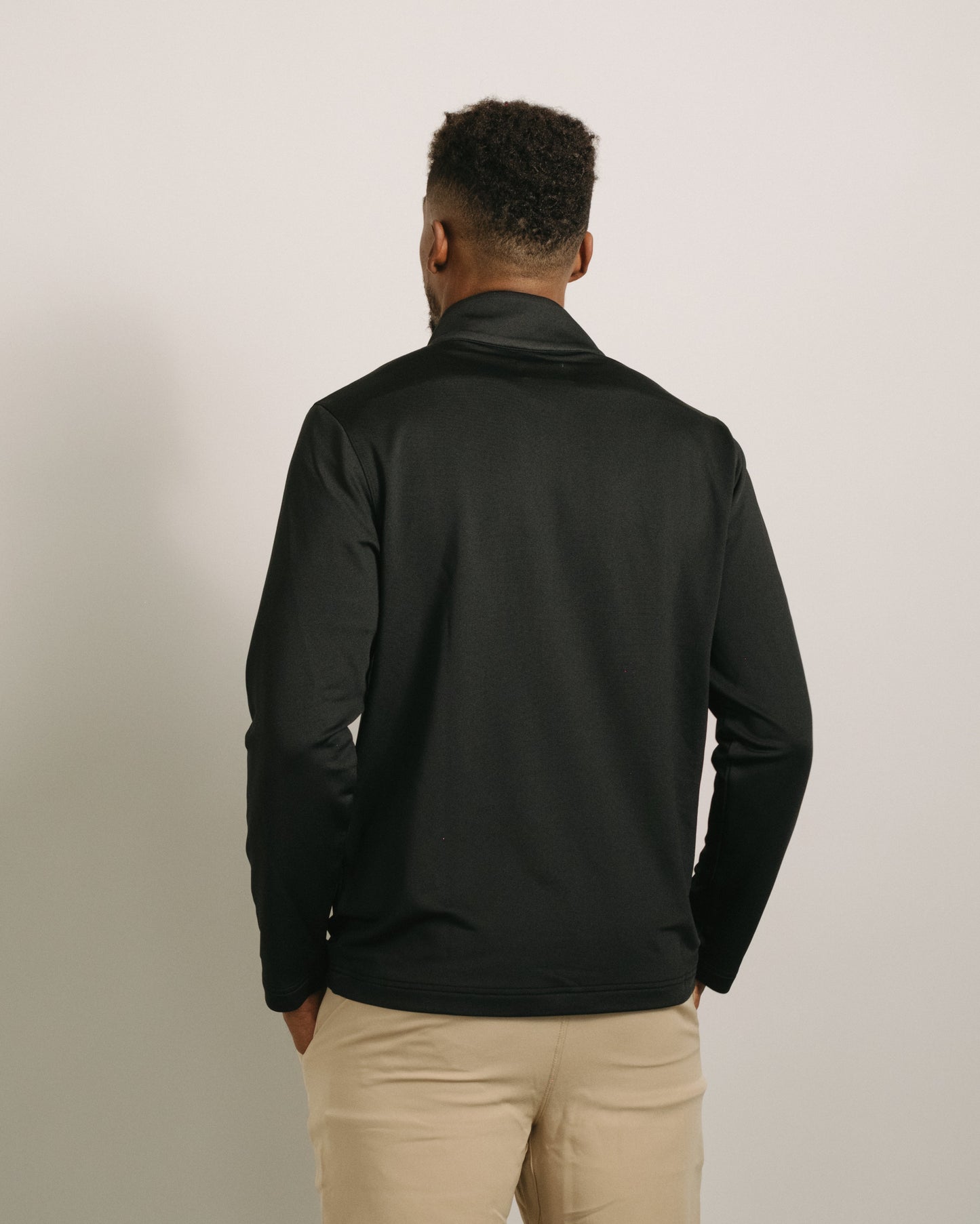 Person wearing a jet black long-sleeve quarter zip and beige pants against a neutral background