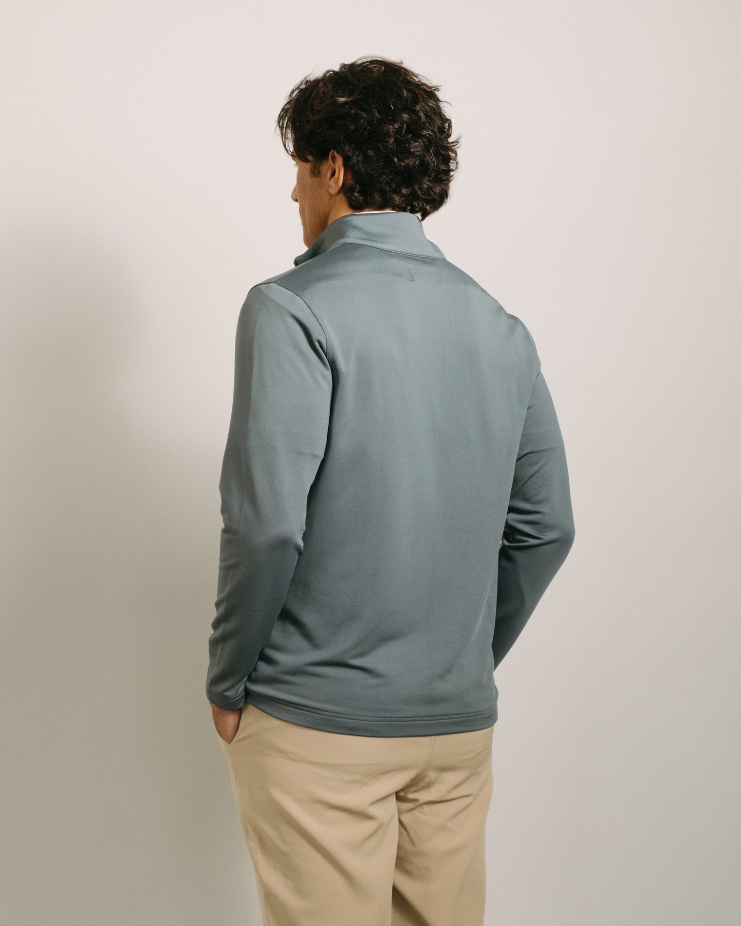 Back angle: Person wearing a steel gray long-sleeve quarter zip a neutral background