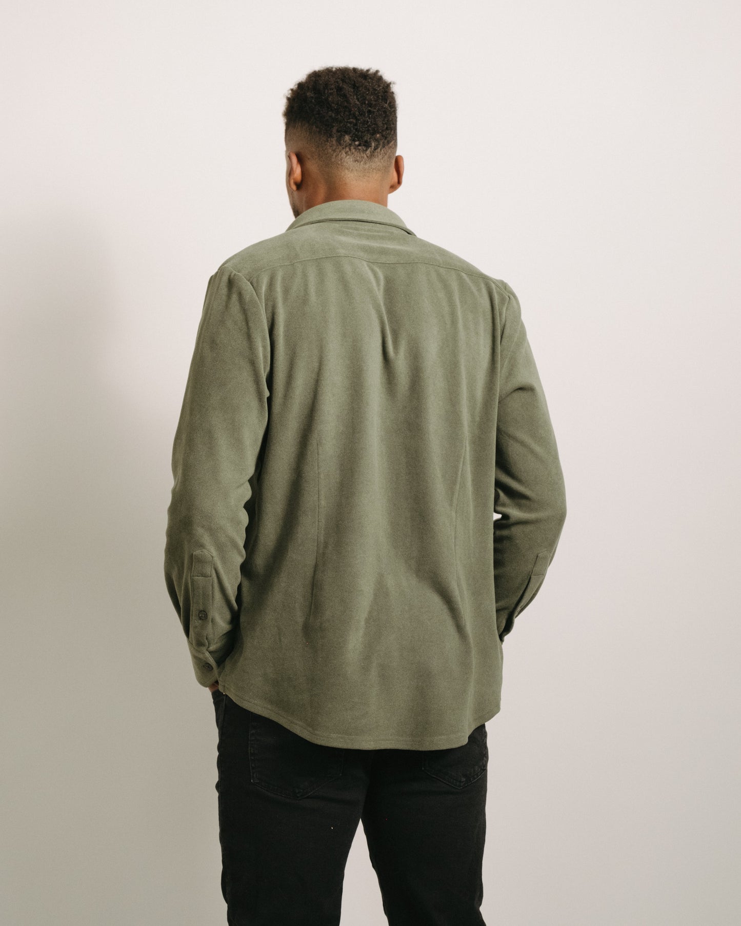 Back angle: Person wearing a pine green flannel and black pants against a plain background