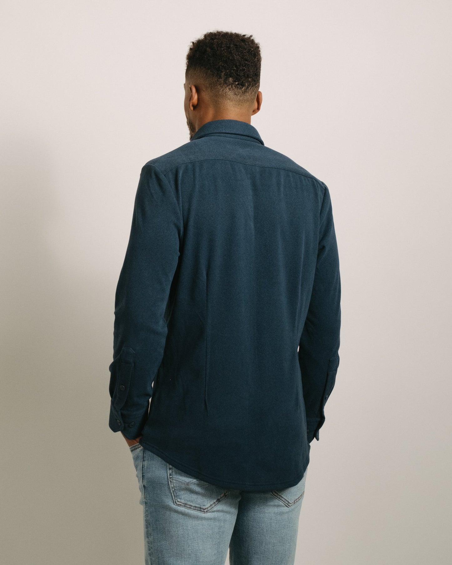 Back angle: Man wearing a storm blue flannel button-up shirt and light blue jeans against a plain background