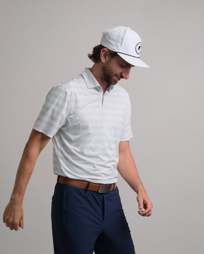 Man wearing a white and gray striped short-sleeve polo shirt, navy pants, and a white cap