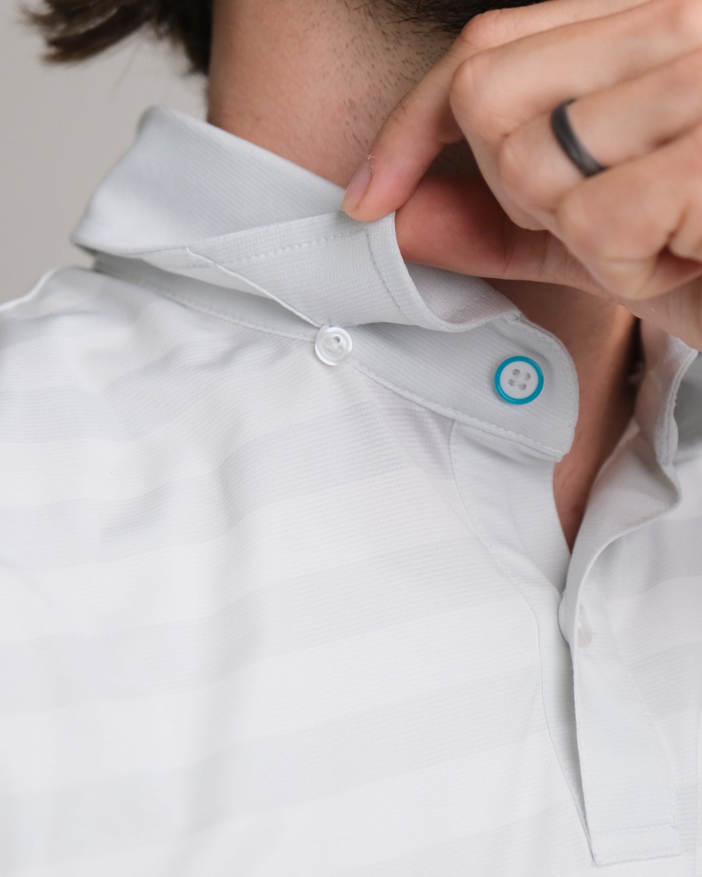 Close up white and gray striped short-sleeve polo shirt, showing colored top button ring and hidden button