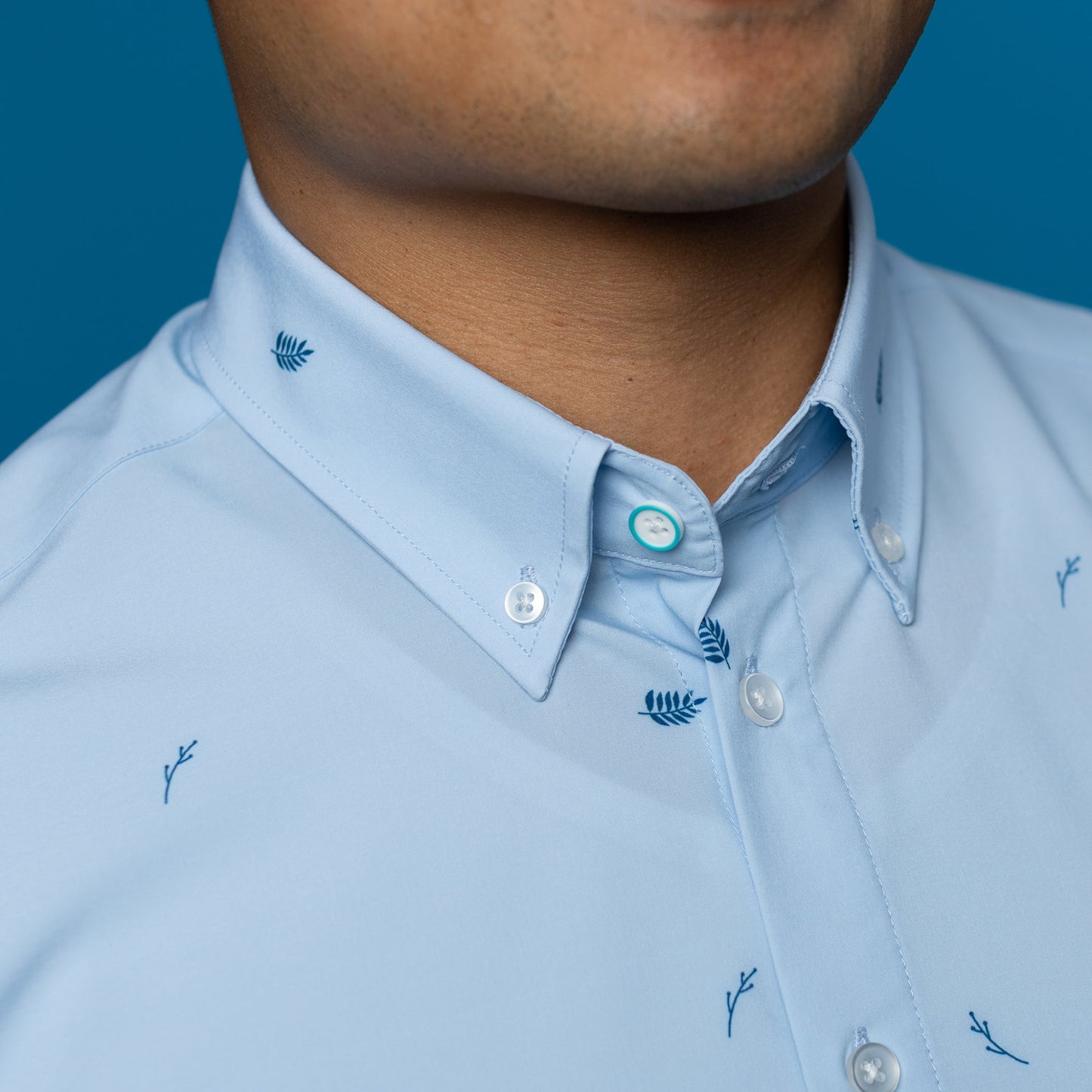 Detail of pale blue shirt with leaves. Button down collar, top button has blue ring
