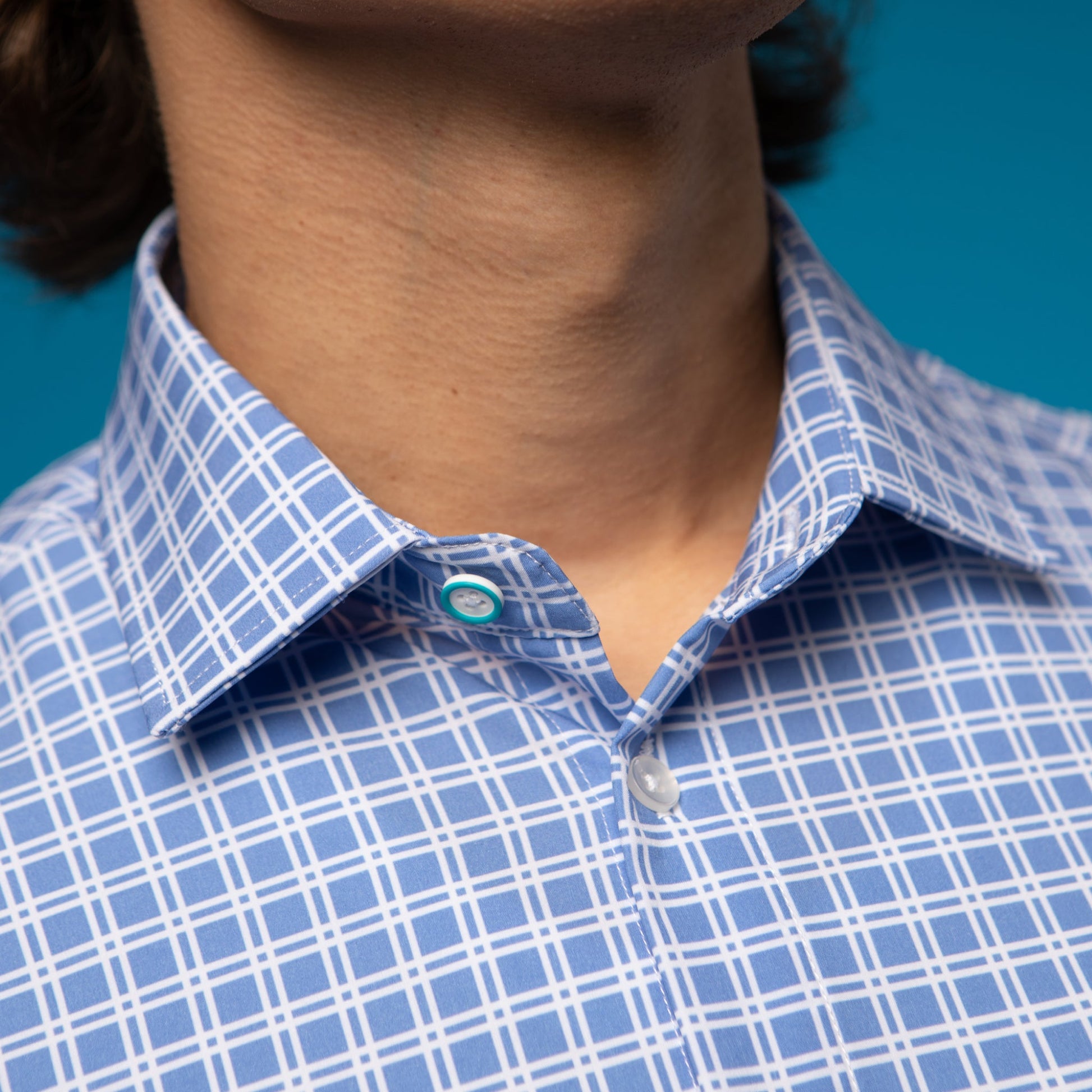 Man wearing Blue shirt with white checkers. Top button has blue ring.