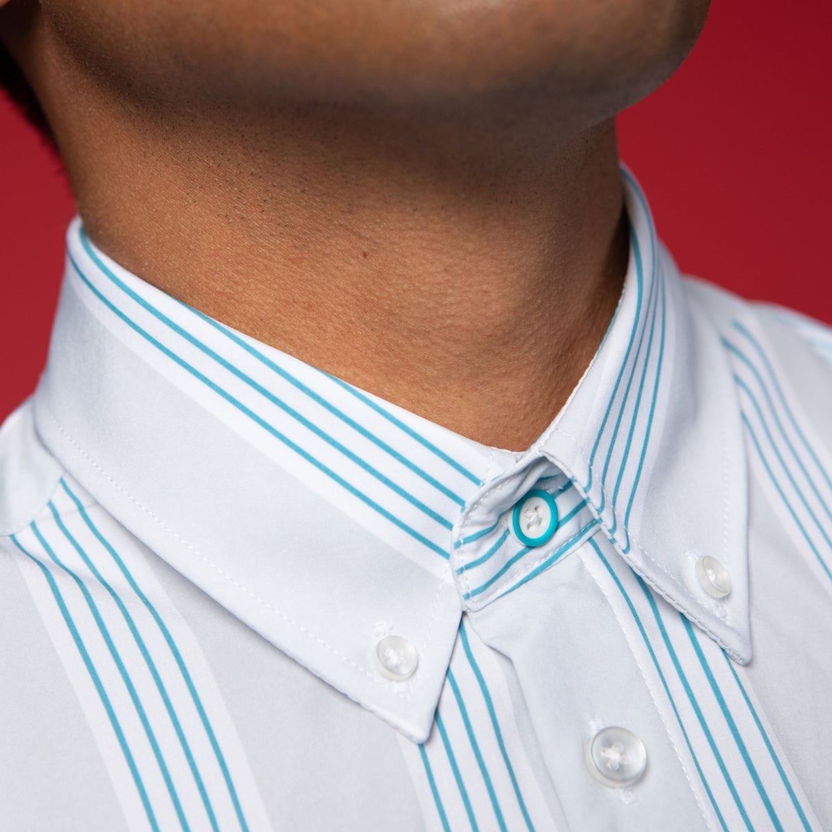 Man wearing Grey shirt with blue and white stripes. Top button has blue ring