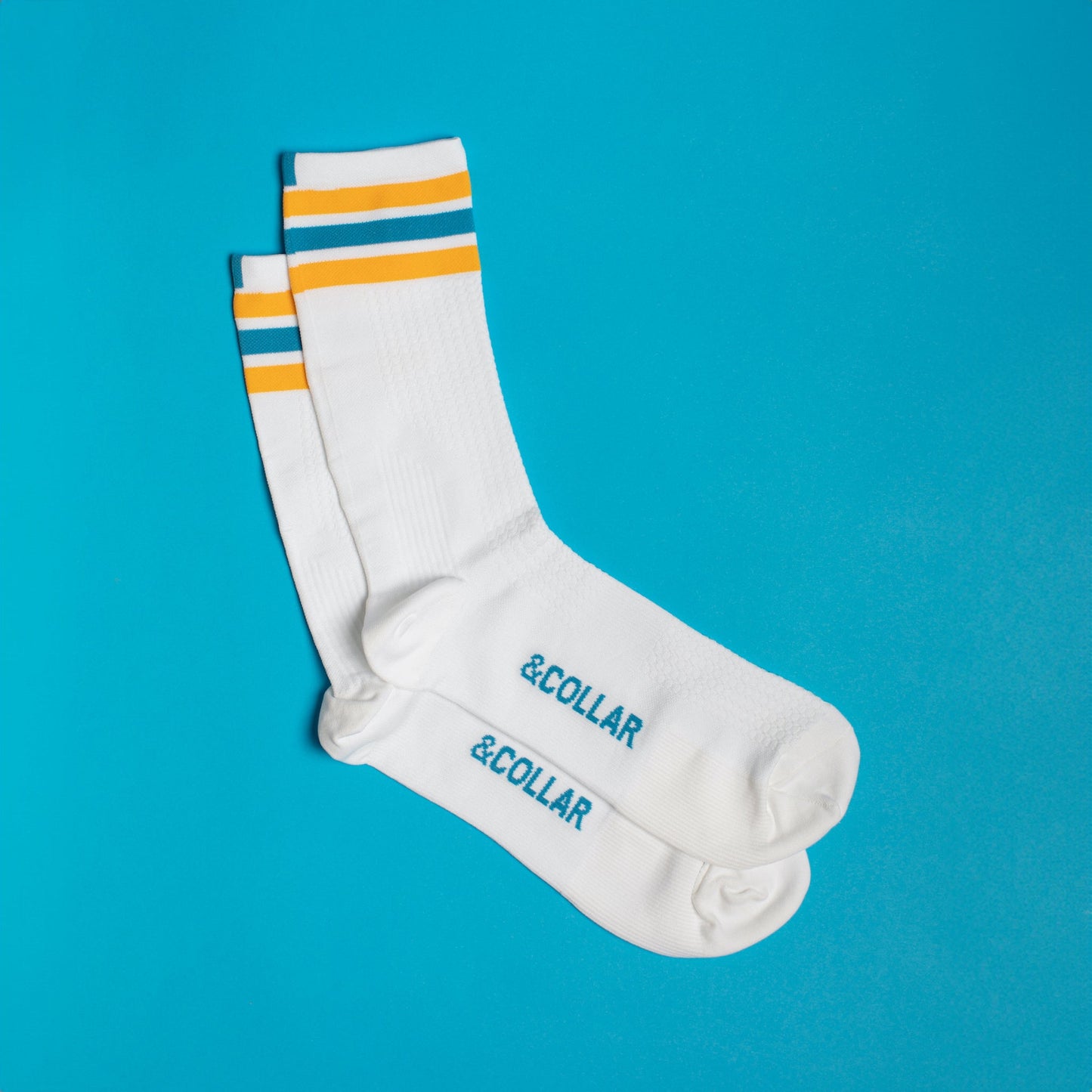 White dress socks with light blue &Collar logo on the bottom, and blue, yellow, and white stripes across the top of the sock.